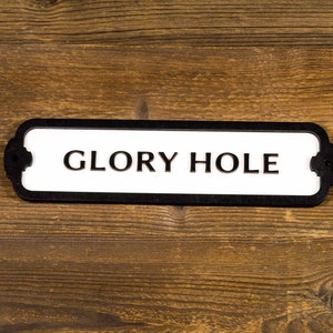 May include: A black and white sign with the text "GLORY HOLE" on a wooden background.