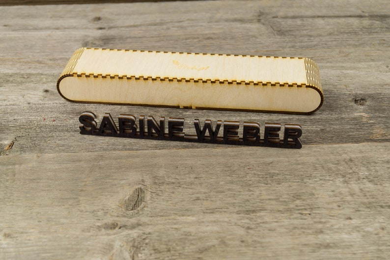 May include: A wooden box with the name "SABINE WEBER" engraved on it. The box is made of light wood and has a simple design.