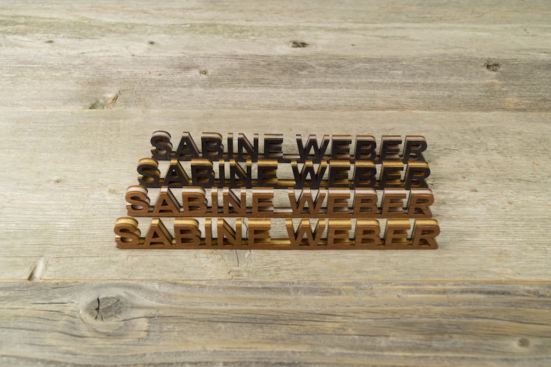 May include: Four wooden name plaques stacked on top of each other, each with the name "Sabine Weber" in black and gold letters.