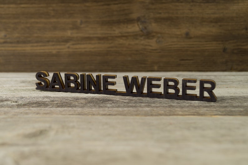 May include: A wooden sign with the name "SABINE WEBER" spelled out in black letters.