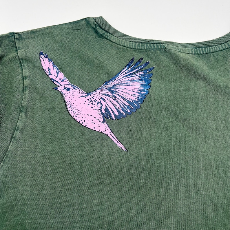 May include: A green t-shirt with a pink and black bird graphic printed on the back.