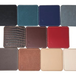 Op de afbeelding: Twaalf vierkante leren onderzetters in verschillende kleuren en texturen, waaronder zwart, teal, marineblauw, grijs, bruin, rood, beige en wit.