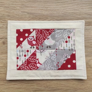 Könnte beinhalten: Ein weißer Stoffuntersetzer mit einem roten, weißen und grauen Patchwork-Design mit Eulen, Vögeln und Blättern. Der Untersetzer ist mit weißem Garn genäht.