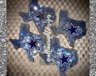 May include: Four Texas-shaped coasters with a glittery blue and silver design. Each coaster features a navy blue star in the center, with the Dallas Cowboys logo. The text "@alliewrightdesigns" is visible on the coasters.