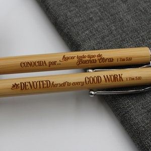 May include: Two bamboo pens with silver accents. The top pen has the text "CONOCIDA por... hacer todo tipo de Buenas Obras 1 Tim 5:10" engraved on it. The bottom pen has the text "she DEVOTED herself to every GOOD WORK 1 Tim 5:10" engraved on it.