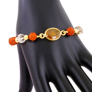 May include: A gold bracelet with a brown oval gemstone, red and white beads, and a gold clasp.