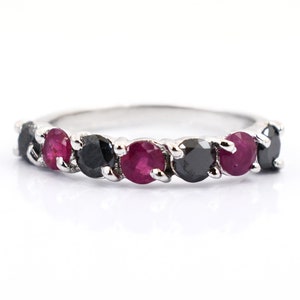 May include: A silver ring featuring alternating round-cut gemstones. The ring showcases a pattern of black and ruby-colored stones, creating a striking contrast. The gemstones are set closely together, enhancing the ring's overall design and appeal.