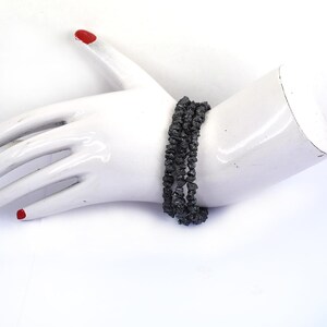 May include: A black beaded bracelet made of rough, faceted stones. The bracelet is layered and appears to be made of multiple strands of beads.