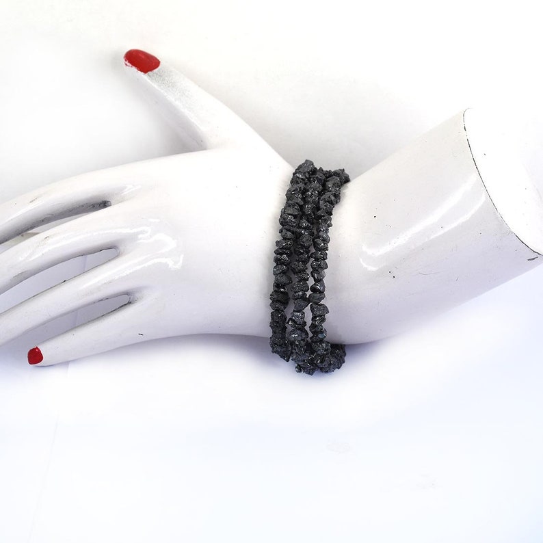 May include: A black beaded bracelet made of rough, faceted stones. The bracelet is layered and appears to be made of multiple strands of beads.