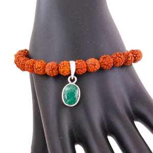 May include: A brown beaded bracelet with a silver pendant featuring a green oval gemstone.