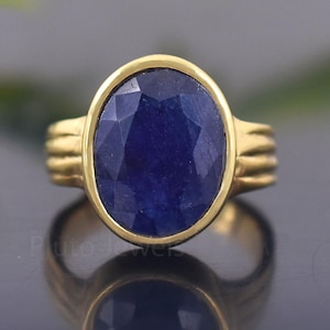 May include: A gold ring with a large, oval-shaped blue sapphire gemstone. The ring has a simple, elegant design.