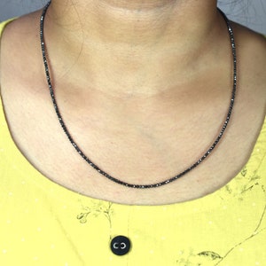 Op de afbeelding: Een zwarte diamanten ketting met kleine, gefacetteerde kralen. De ketting wordt gedragen door een persoon met een geel shirt.