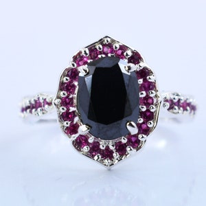May include: A silver ring with a large black oval gemstone surrounded by a halo of smaller pink gemstones.