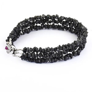 May include: A black diamond bracelet with a silver clasp. The bracelet is made of multiple strands of small, rough black diamonds.