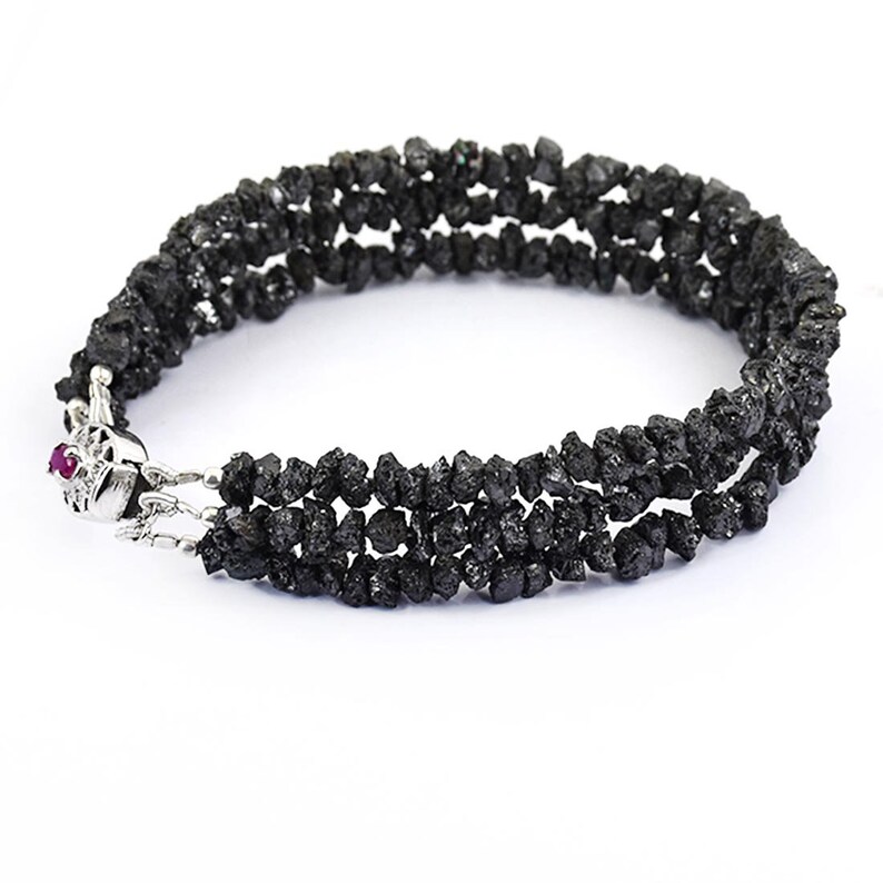 May include: A black diamond bracelet with a silver clasp. The bracelet is made of multiple strands of small, rough black diamonds.