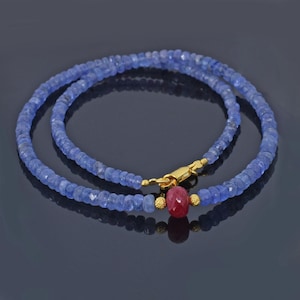 May include: A double-strand necklace made of blue gemstone beads with a gold clasp and a single red gemstone pendant.