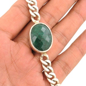 May include: A silver chain bracelet with a large, oval-shaped green gemstone.