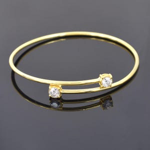 Peut inclure: Un bracelet jonc doré avec deux pierres précieuses rondes et transparentes. Le bracelet a un design simple et élégant avec une surface lisse et réfléchissante. Les pierres sont serties dans des lunettes carrées, ajoutant une touche d'éclat.