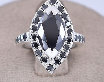 May include: A silver ring with a large marquise-shaped black gemstone surrounded by a halo of smaller black gemstones.