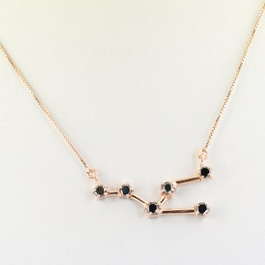 Könnte beinhalten: Halskette aus Roségold mit einem Sternbild-Design mit schwarzen Edelsteinen. Die Kette hat eine zarte Kette und ein geometrisches Muster, perfekt für den Alltag oder besondere Anlässe.