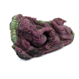 May include: A carved stone sculpture of a deity, featuring a deep magenta color with green accents. The sculpture depicts a figure with an elephant head and multiple arms, a common representation of the Hindu god Ganesha.