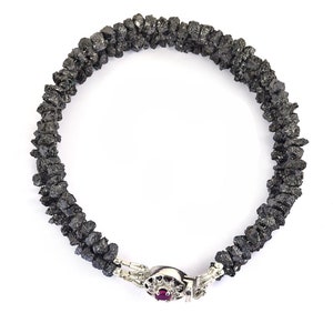 May include: A black diamond bracelet with a silver clasp featuring a small red gemstone. The bracelet is made of rough, uncut black diamonds.