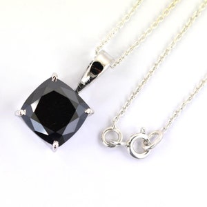Peut inclure: Un collier en argent avec un pendentif carré en pierre noire. Le pendentif est maintenu par quatre griffes et suspendu à une fine chaîne en argent. Le fermoir est visible. Le fond est blanc.