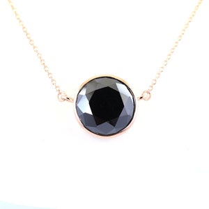 May include: A rose gold necklace featuring a large, round, faceted black gemstone pendant. The pendant is set in a bezel setting and hangs from a delicate chain. The gemstone reflects light, creating a sparkling effect. The necklace is displayed against a white background.