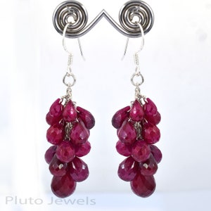 May include: A pair of dangle earrings with a cluster of ruby red gemstone drops hanging from each earring. The earrings are made of sterling silver.