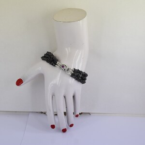 May include: A multi-strand bracelet made of black beads with a silver clasp featuring a pink gemstone.
