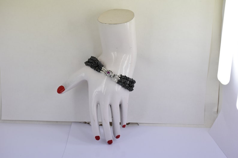 May include: A multi-strand bracelet made of black beads with a silver clasp featuring a pink gemstone.