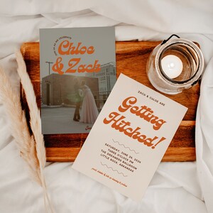 Puede incluir: Invitaci&oacute;n de boda con un dise&ntilde;o retro. La invitaci&oacute;n presenta una foto de la pareja frente a un edificio con el texto "Chloe & Zack" en una fuente naranja en negrita. La invitaci&oacute;n tambi&eacute;n incluye el texto "Getting Hitched!" en una fuente similar. La invitaci&oacute;n est&aacute; colocada sobre una superficie de madera con una vela en un frasco de vidrio.