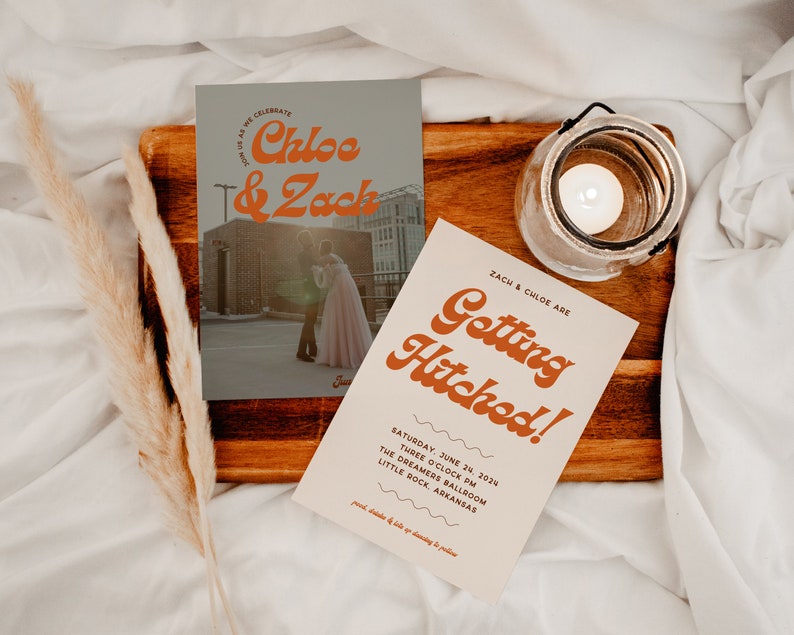 Puede incluir: Invitaci&oacute;n de boda con un dise&ntilde;o retro. La invitaci&oacute;n presenta una foto de la pareja frente a un edificio con el texto "Chloe & Zack" en una fuente naranja en negrita. La invitaci&oacute;n tambi&eacute;n incluye el texto "Getting Hitched!" en una fuente similar. La invitaci&oacute;n est&aacute; colocada sobre una superficie de madera con una vela en un frasco de vidrio.