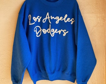 May include: A royal blue sweatshirt with a white glitter design that reads "Los Angeles Dodgers".