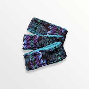 May include: A set of three fleece headbands with a teal, purple, and black geometric pattern.
