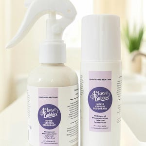 May include: Two white bottles of plant-based liquid deodorant. One bottle has a spray nozzle, the other has a cap. Both bottles have a purple label with the text "4 Love & Bubbles" and "Liquid Casual Deodorant".