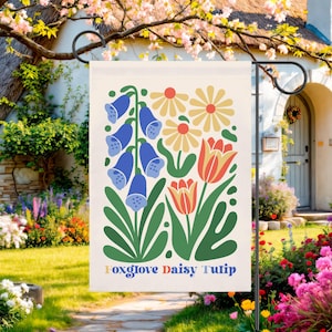 May include: A garden flag featuring a floral design with blue foxgloves, yellow daisies, and red tulips. The words "Foxglove Daisy Tulip" are printed at the bottom in a colorful font. The flag is displayed on a black metal stand.