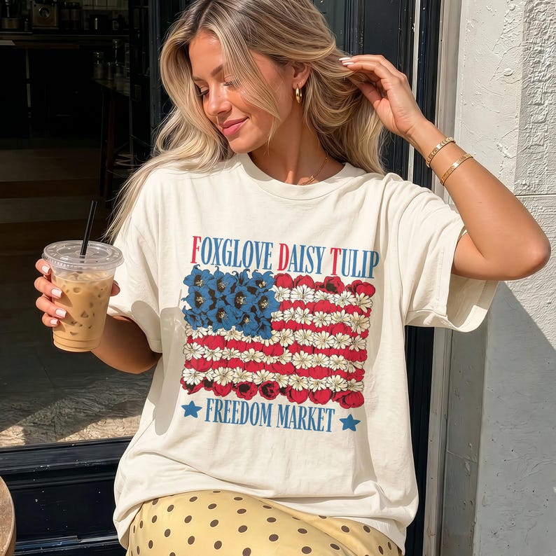 Cream t-shirt with American flag design featuring daisies and tulips, "Freedom Market" text.
