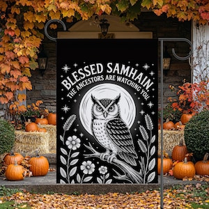 May include: Black garden flag with a white owl perched on a branch in front of a full moon. The flag reads "Blessed Samhain, The Ancestors Are Watching You" in white text. Pumpkins and fall foliage surround the flag.