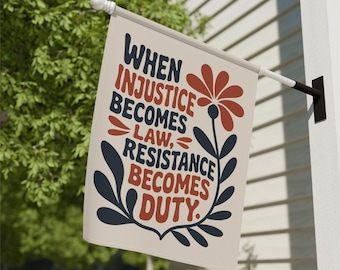 May include: A rectangular flag with the text "WHEN INJUSTICE BECOMES LAW, RESISTANCE BECOMES DUTY." The flag has a cream background with a floral design in red and navy blue. The flag is hanging outside.