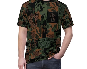 May include: A short-sleeved t-shirt with a camouflage pattern in shades of green, brown, and black. The design incorporates QR codes and a black square with a white fist graphic. The shirt has a black crew neck.