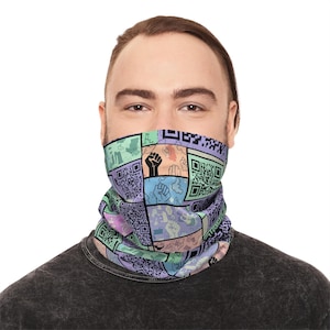 May include: A multi-colored face covering with a patchwork design. The design includes QR codes, raised fists, and other graphics in shades of purple, green, blue, and orange. The face covering is worn by a person with light skin and dark hair.