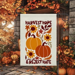 May include: A rectangular garden flag with a cream background featuring two orange pumpkins, yellow and dark red sunflowers, and autumn leaves. The text HARVEST HOPE & REJECT HATE is printed in dark red at the top and bottom of the design.