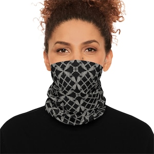 May include: A black and white patterned neck gaiter. The neck gaiter features a geometric design with diamond and square shapes. The person in the image is wearing a black top.