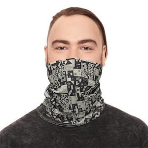 May include: A black and beige patterned neck gaiter. The design features geometric shapes and QR code-like patterns. The neck gaiter is worn around the neck and covers the lower face. The person in the image is wearing a dark gray shirt.