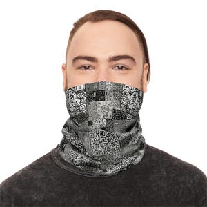May include: A gray and black face covering with a patchwork design. The design includes squares with QR codes and other geometric patterns. The face covering is worn by a person.