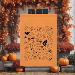 Könnte beinhalten: Orangene Halloween-Gartenflagge mit schwarzen Illustrationen von Kürbissen, Fledermäusen, Hexenhüten, Geistern und anderen gruseligen Symbolen. Die Flagge hängt an einem schwarzen Metallständer, mit Kürbissen und Herbstlaub im Hintergrund.
