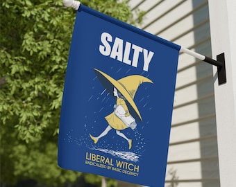 May include: A blue flag with the word "SALTY" in white at the top. Below is an illustration of a witch in a yellow dress and hat, carrying a salt shaker. The text "LIBERAL WITCH RADICALIZED BY BASIC DECENCY" is at the bottom.