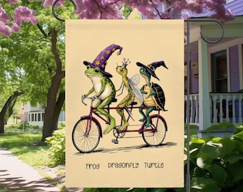May include: A whimsical garden flag features a frog, dragonfly, and turtle riding a tandem bicycle. The frog wears a wizard hat, the dragonfly a crown, and the turtle a witch hat. The flag has the words "FROG DRAGONFLY TURTLE" at the bottom.
