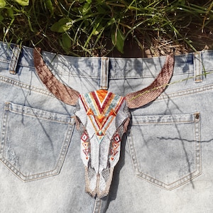 May include: Embroidered bull skull patch with brown horns and colorful geometric patterns in orange, red, and turquoise. The patch is placed on the back pocket of a pair of light blue denim jeans.